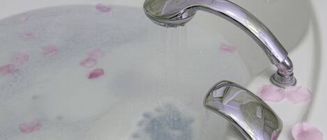 A bathtub with rose petals floating on the water and a chrome faucet.