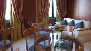 A dining area with a glass table, wooden chairs with patterned cushions, a bowl of fruit, and a sofa with patterned pillows. - AS Hotel Monza (Monza)