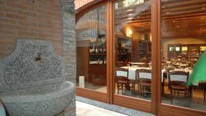 A stone fountain, a brick wall, and a restaurant with tables and chairs visible through a glass door. - AS Hotel Monza (Monza)