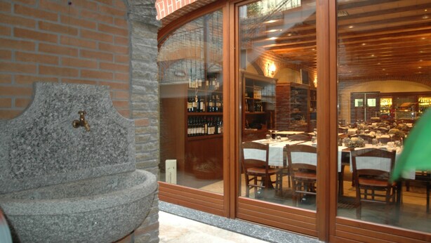 A stone fountain, a brick wall, and a restaurant with tables and chairs visible through a glass door.