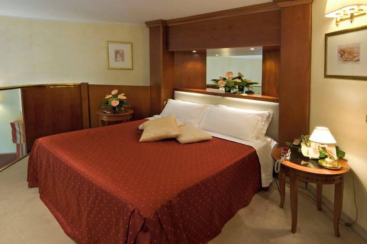 Una habitación de hotel con una cama grande, una mesita de noche con lámpara y un espejo sobre la cama.