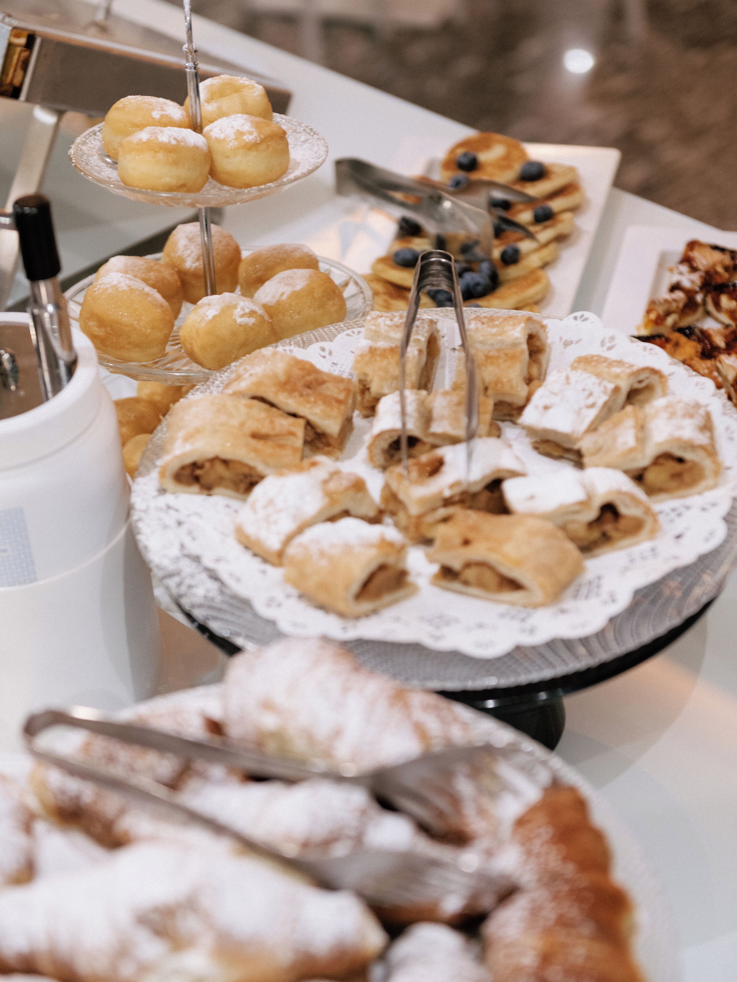 En buffet med forskellige kager og desserter, heriblandt éclairs og en kage med et blondedekor.