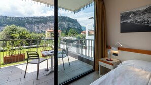 A hotel room with a balcony, a bed, a bedside table, and a view of mountains. - Hotel Holiday Sport & Relax (Nago-Torbole)