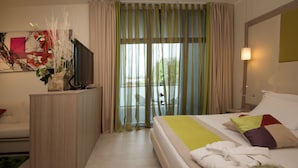 Quarto de hotel com cama, televisão em móvel, escrivaninha e vista para o exterior pela janela.