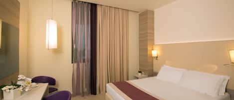 Una habitación de hotel con una cama, un escritorio con sillas, una lámpara y una cortina.