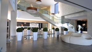 Um lobby espaçoso com escadaria moderna, áreas de estar e um amplo sofá branco.