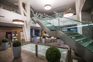 Un intérieur moderne avec un escalier en verre, des espaces de détente et un comptoir d’accueil.