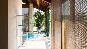 Un área de piscina interior moderna con paredes de vidrio, techo de madera y vistas a zonas verdes.