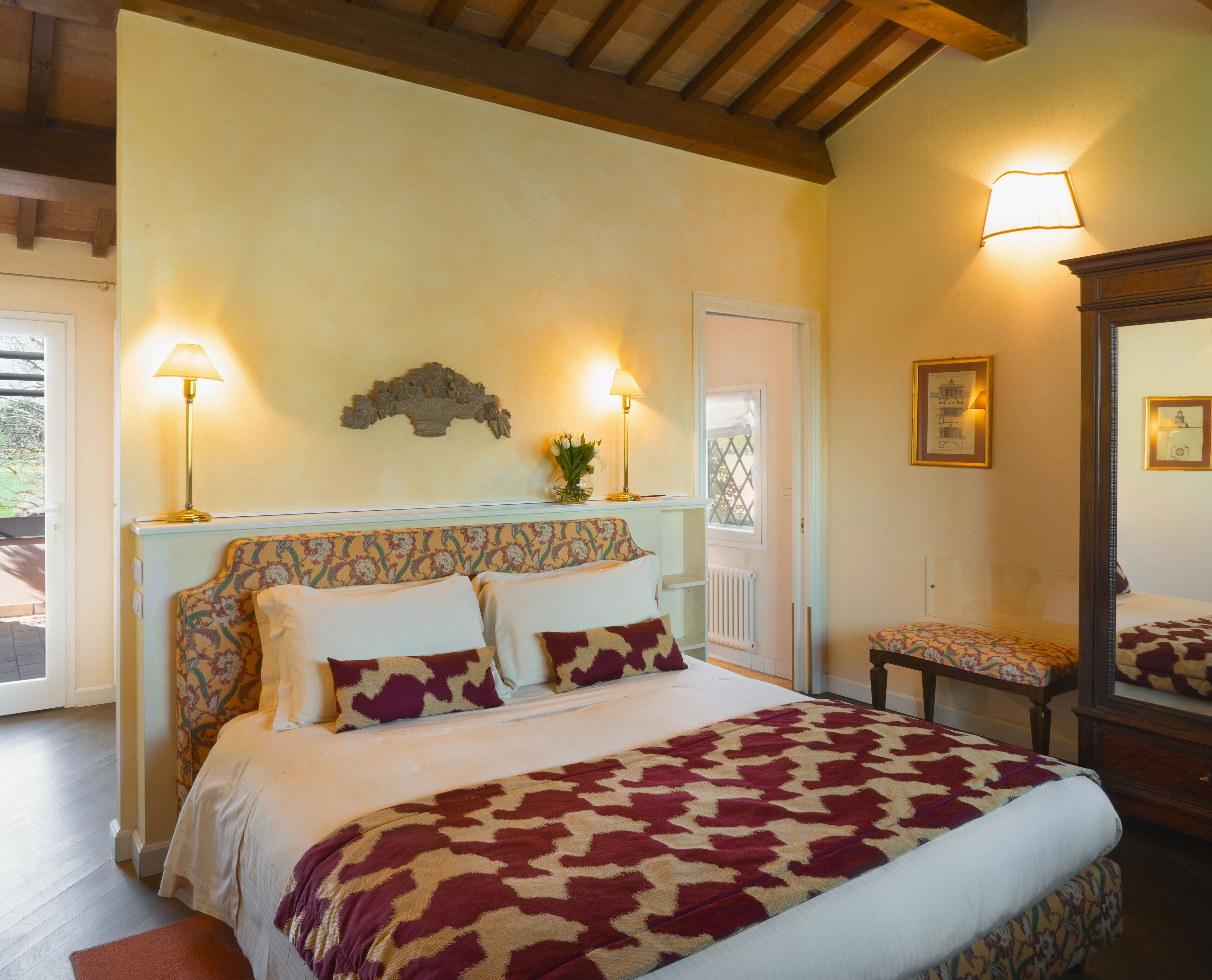 A bedroom with a bed, two bedside lamps, a mirror, and a floral-patterned headboard.