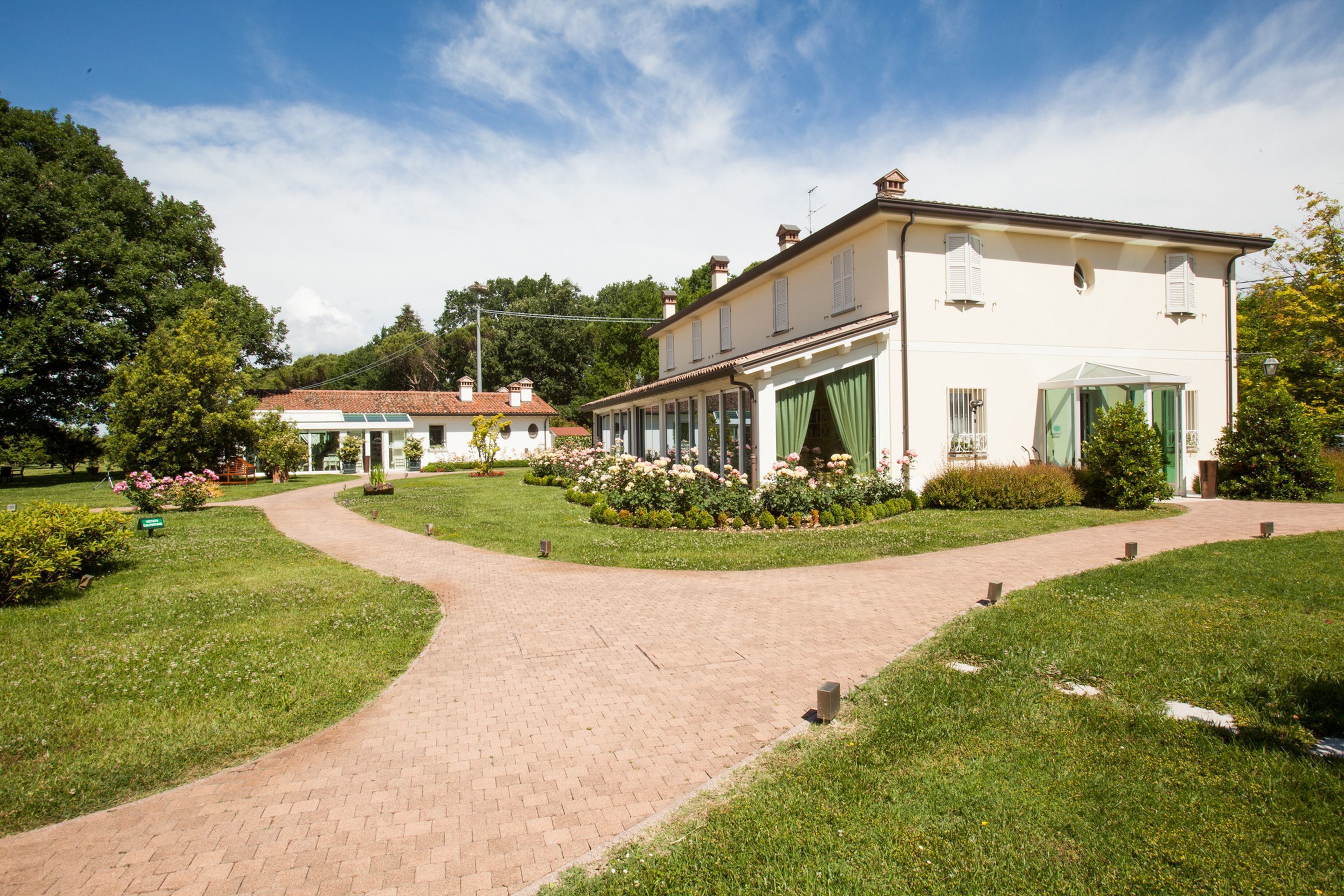 A large, white building with a garden pathway leading to it, surrounded by greenery and flowers.