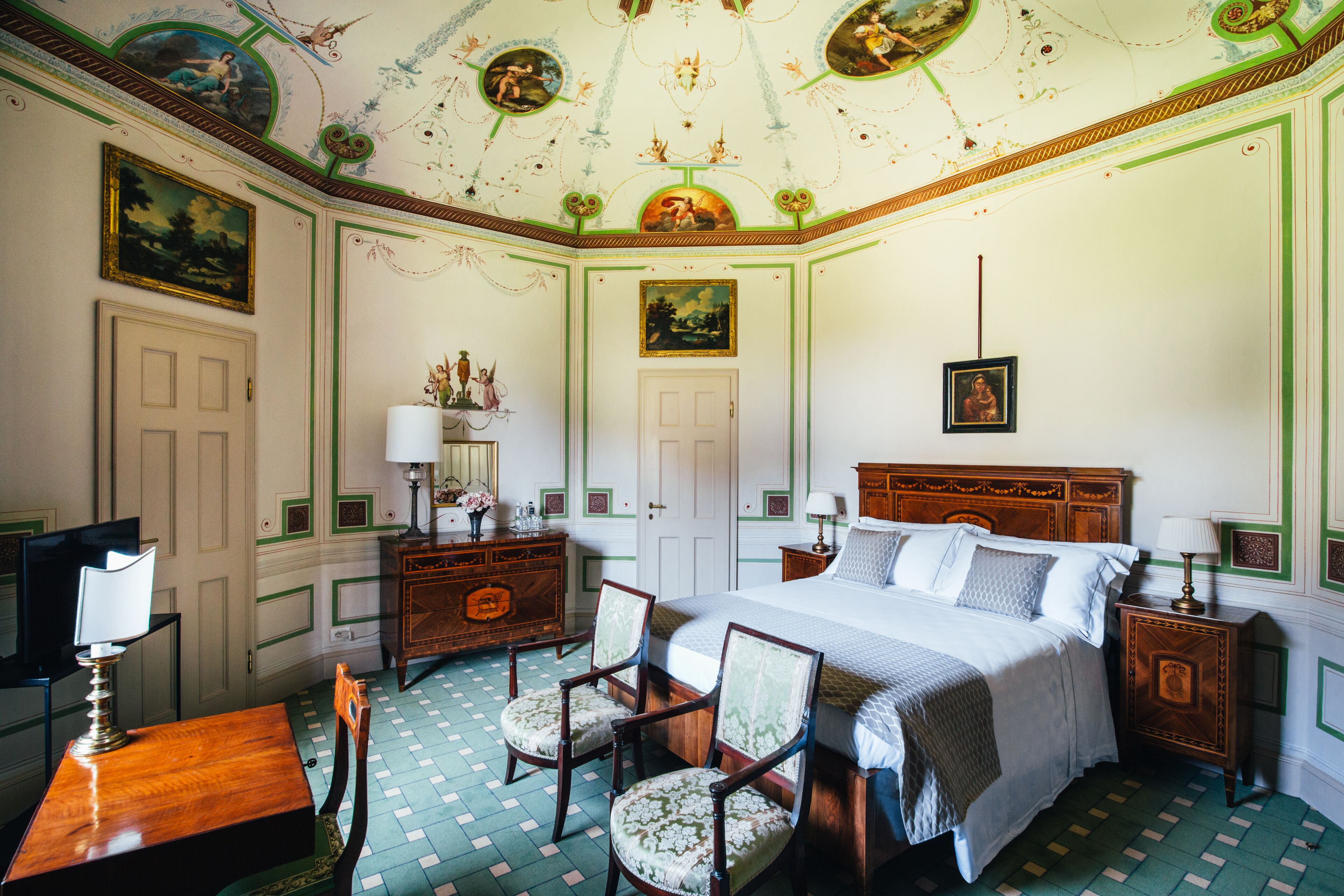 Une chambre avec un grand lit, deux fauteuils, un bureau et un téléviseur.