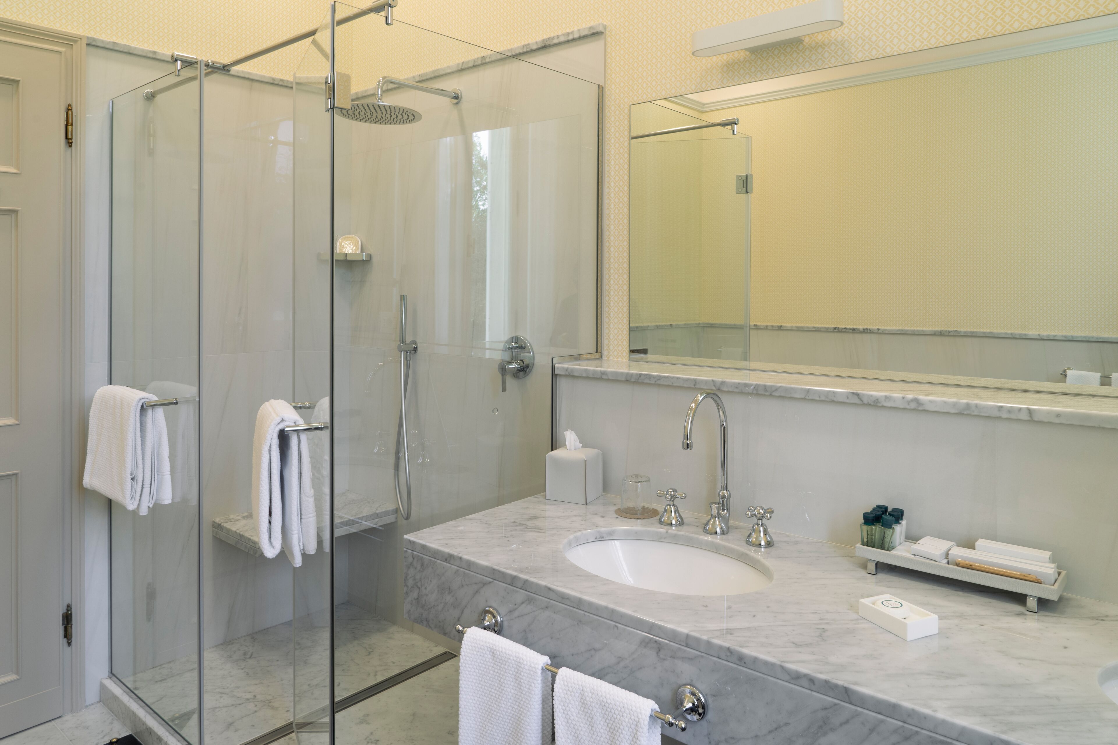 A modern bathroom with a glass-enclosed shower, a marble sink, and a large mirror.
