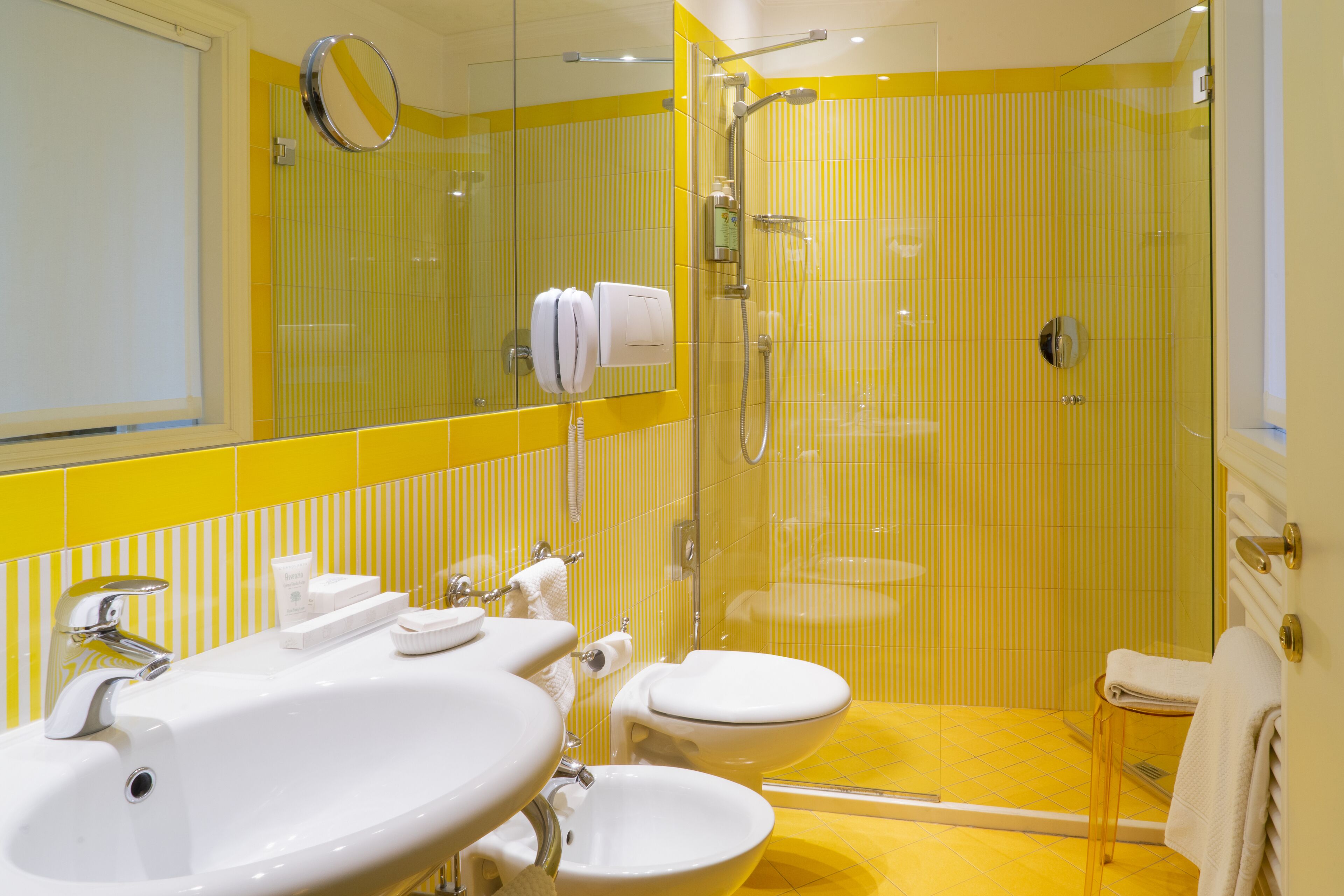 A bathroom with yellow-striped walls, a glass-enclosed shower, a white sink, and a toilet.