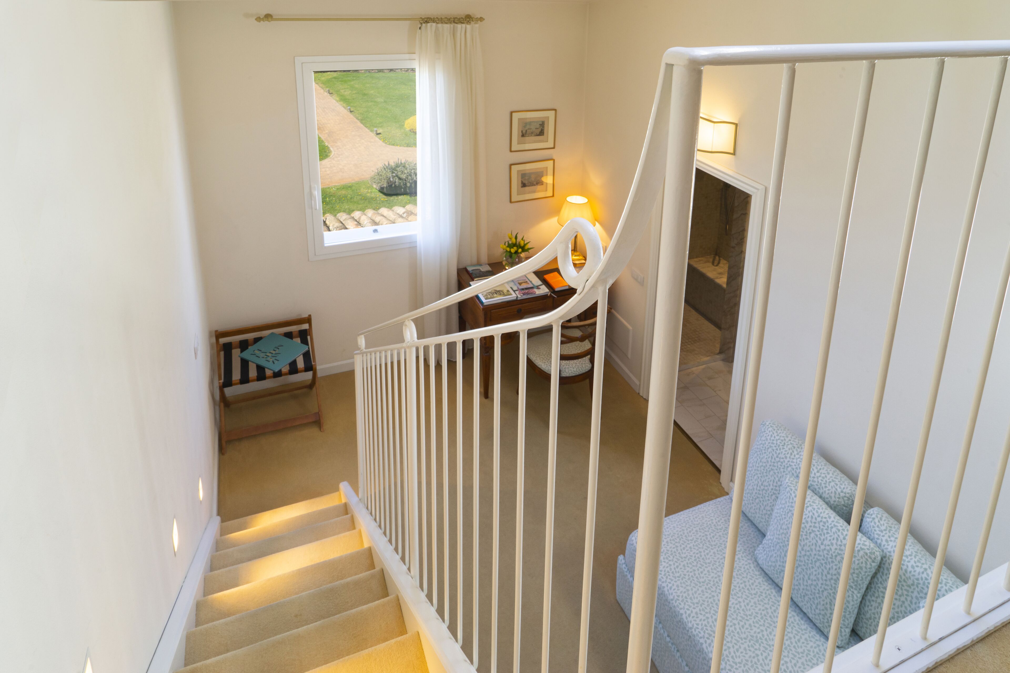 A staircase with a white railing leading to a bedroom with a bed and a nightstand.