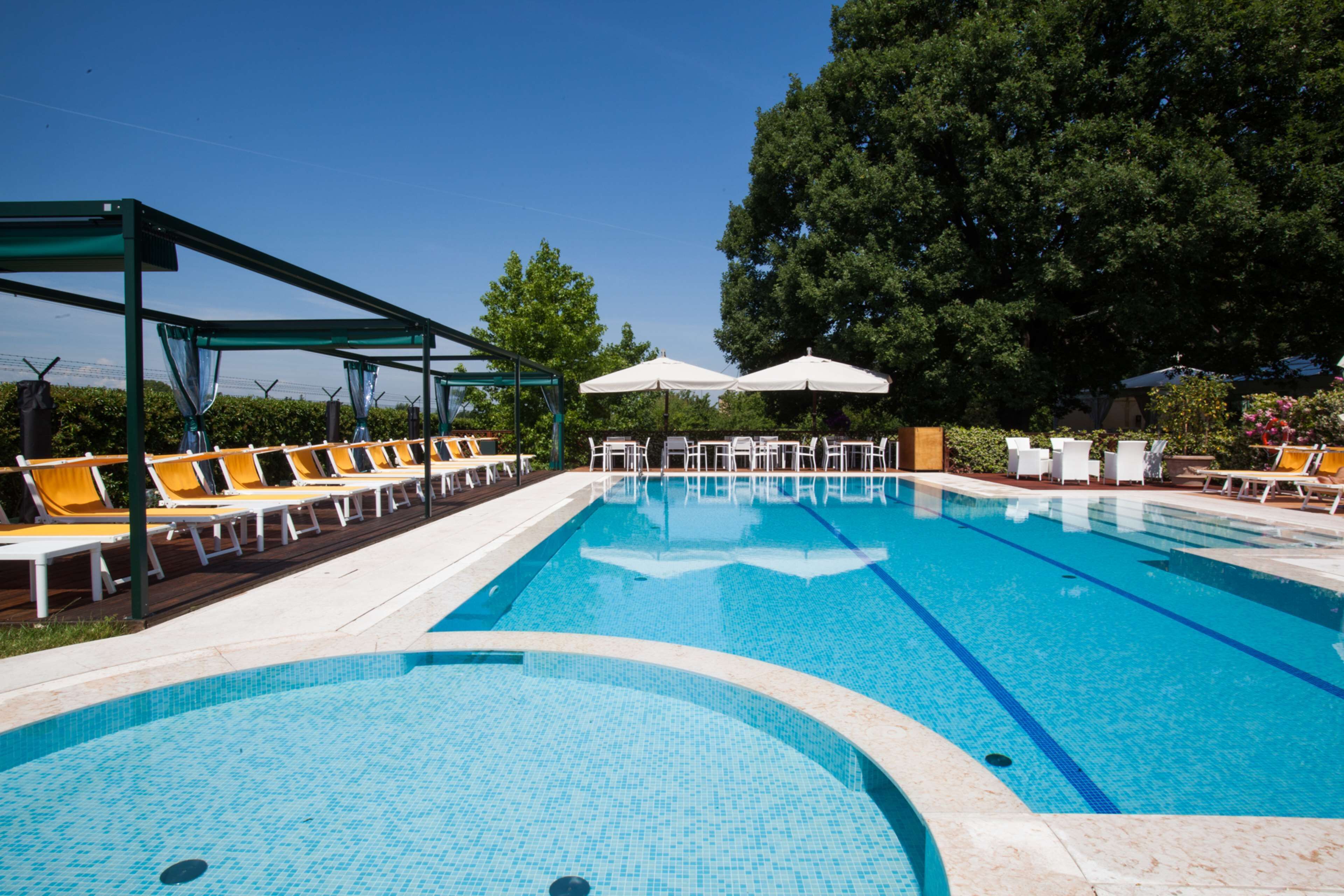 Piscina con sillas de descanso y sombrillas, rodeada de árboles.
