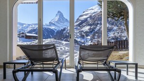 Two lounge chairs facing a large window with a mountain view. - Hotel Alpenroyal (Zermatt)