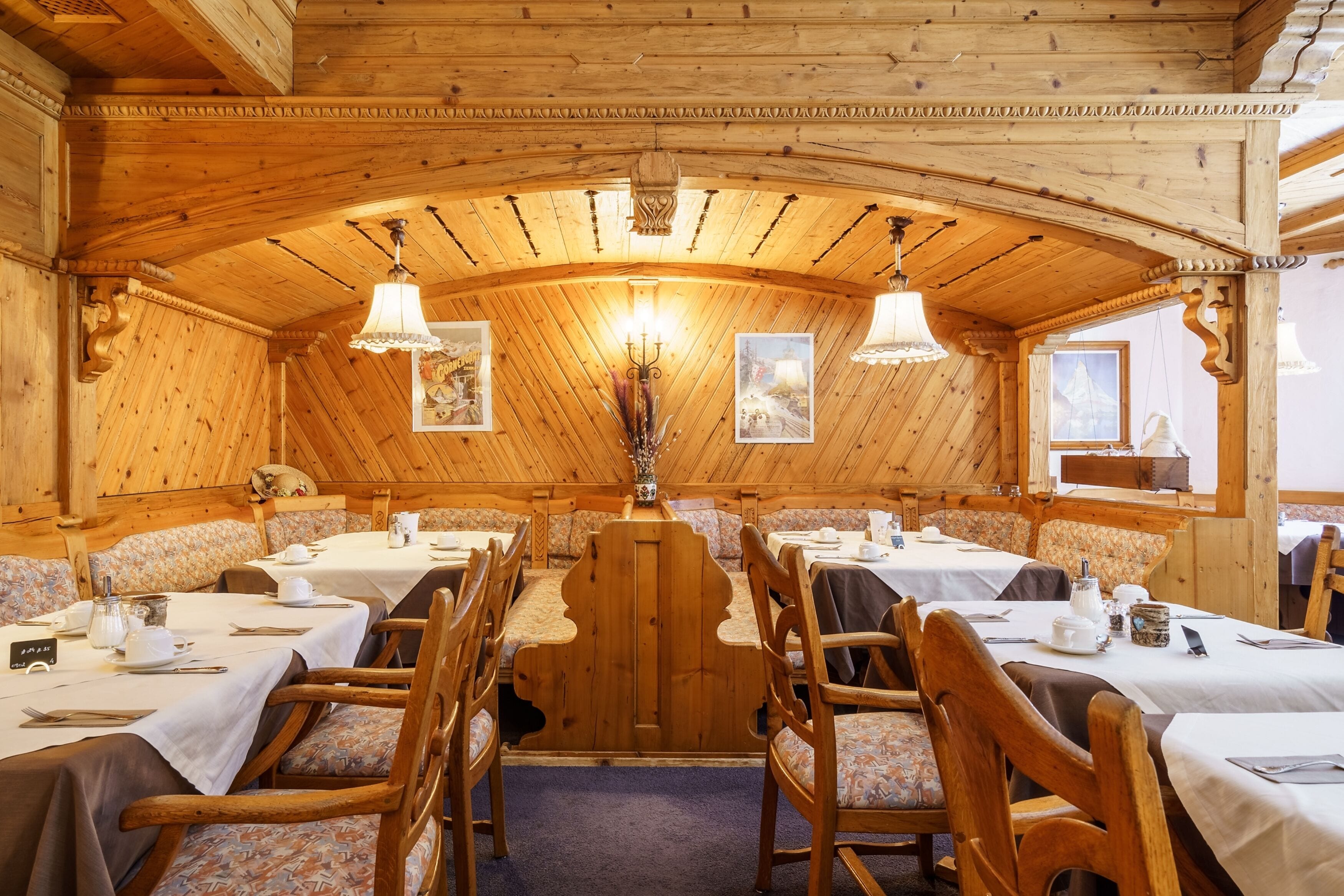 A wooden dining area with tables and benches, decorated with paintings and a chandelier.