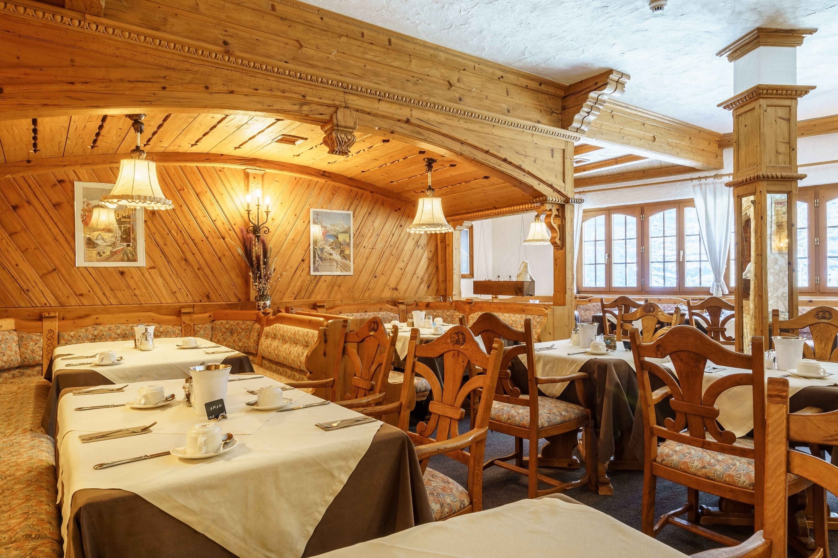 Ein gemütliches, holzgetäfeltes Interieur mit gedeckten Tischen, hölzernen Stühlen und einer hohen Decke mit Holzbalken.