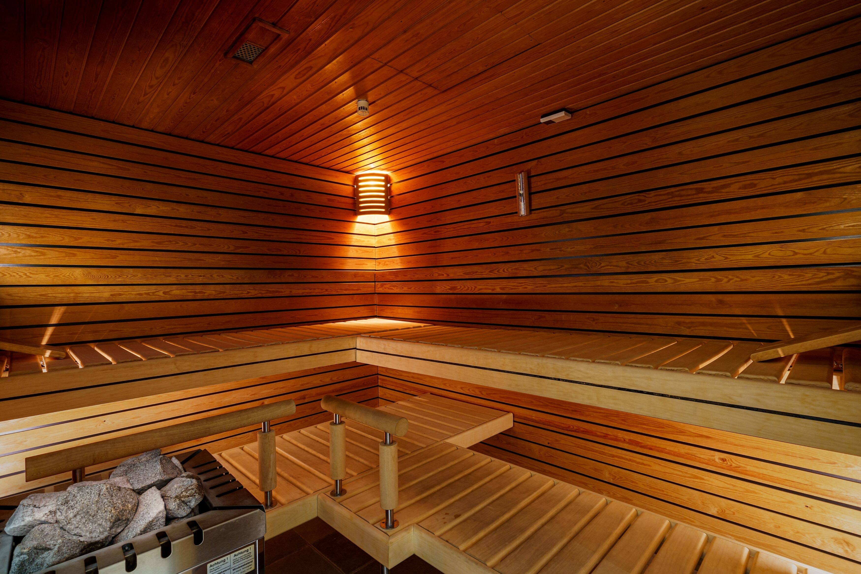A sauna with wooden slats on the ceiling and walls, a bench with a metal frame, and a stone-filled basin at the bottom.