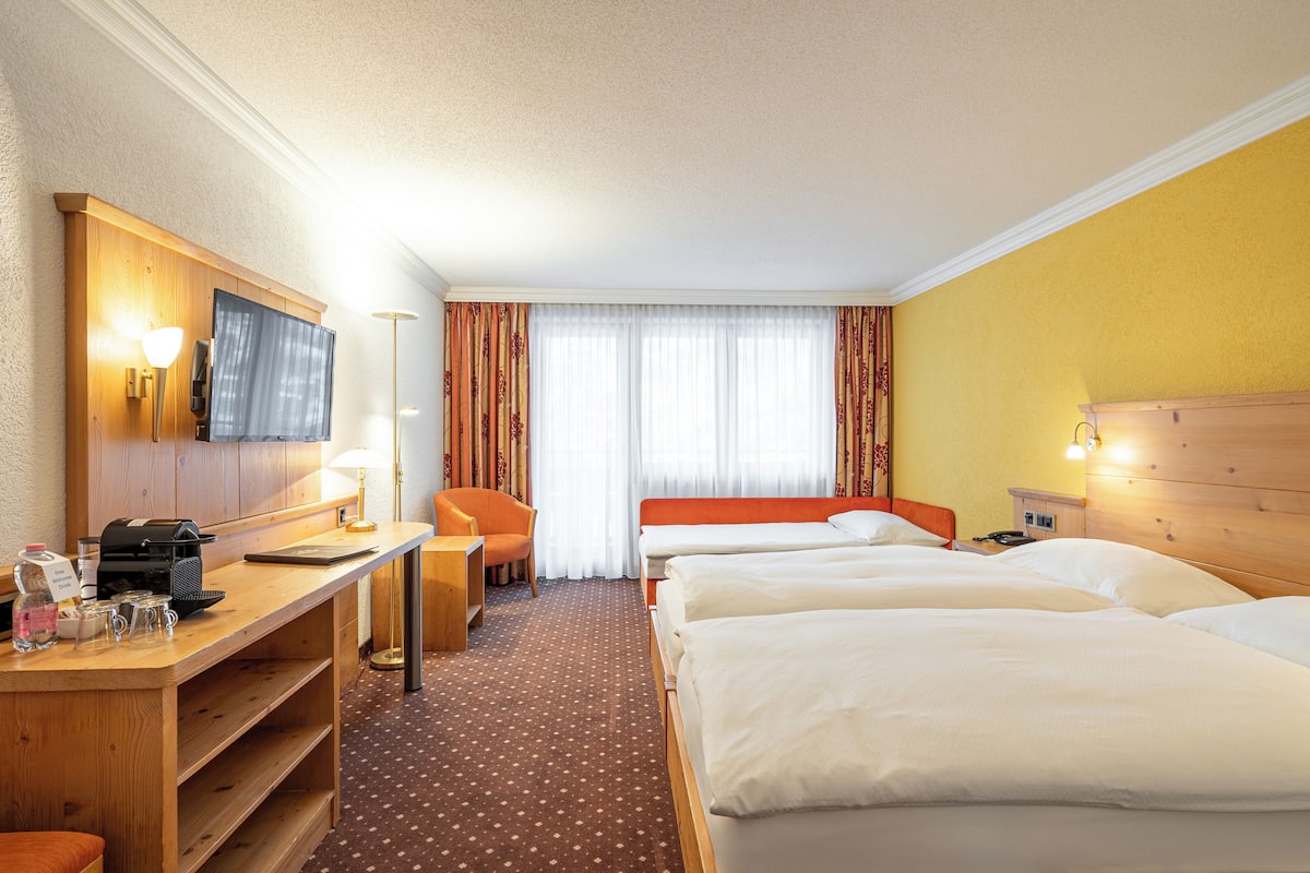 A hotel room with a desk, two beds, a chair, and a TV.