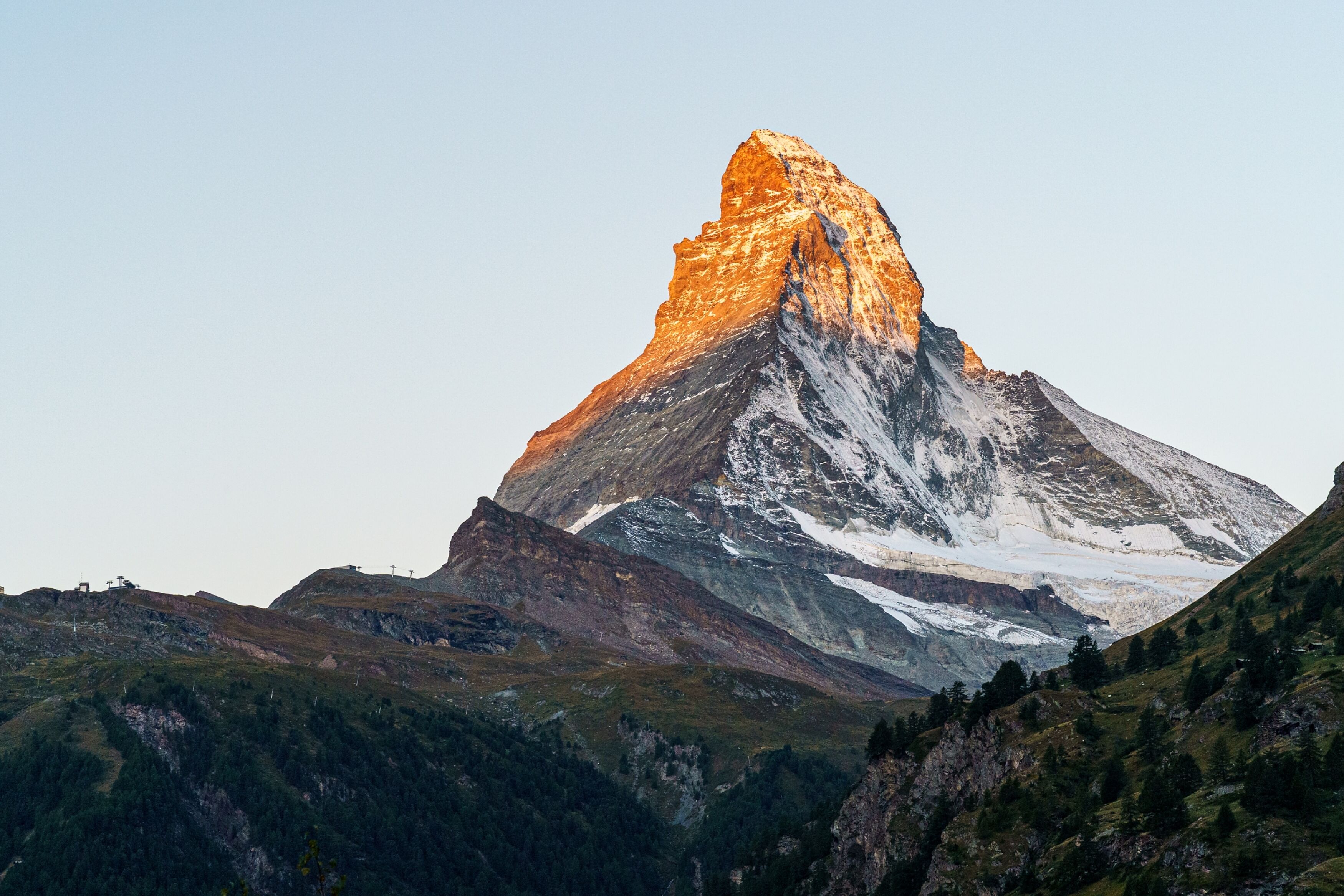 A mountain with a prominent peak, surrounded by forested slopes and a clear sky.