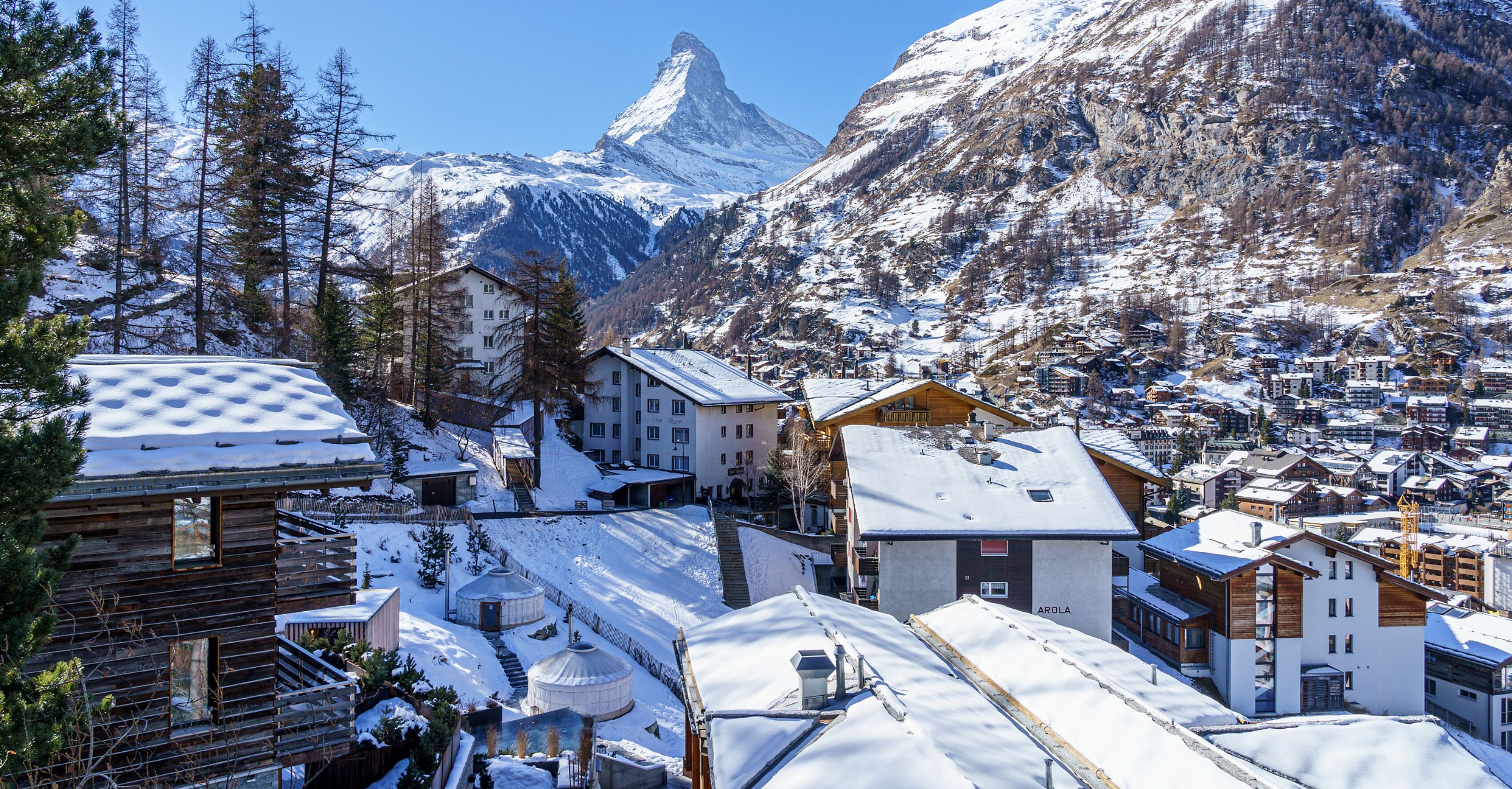 A snow-covered mountain town with wooden buildings and a prominent mountain peak in the background.