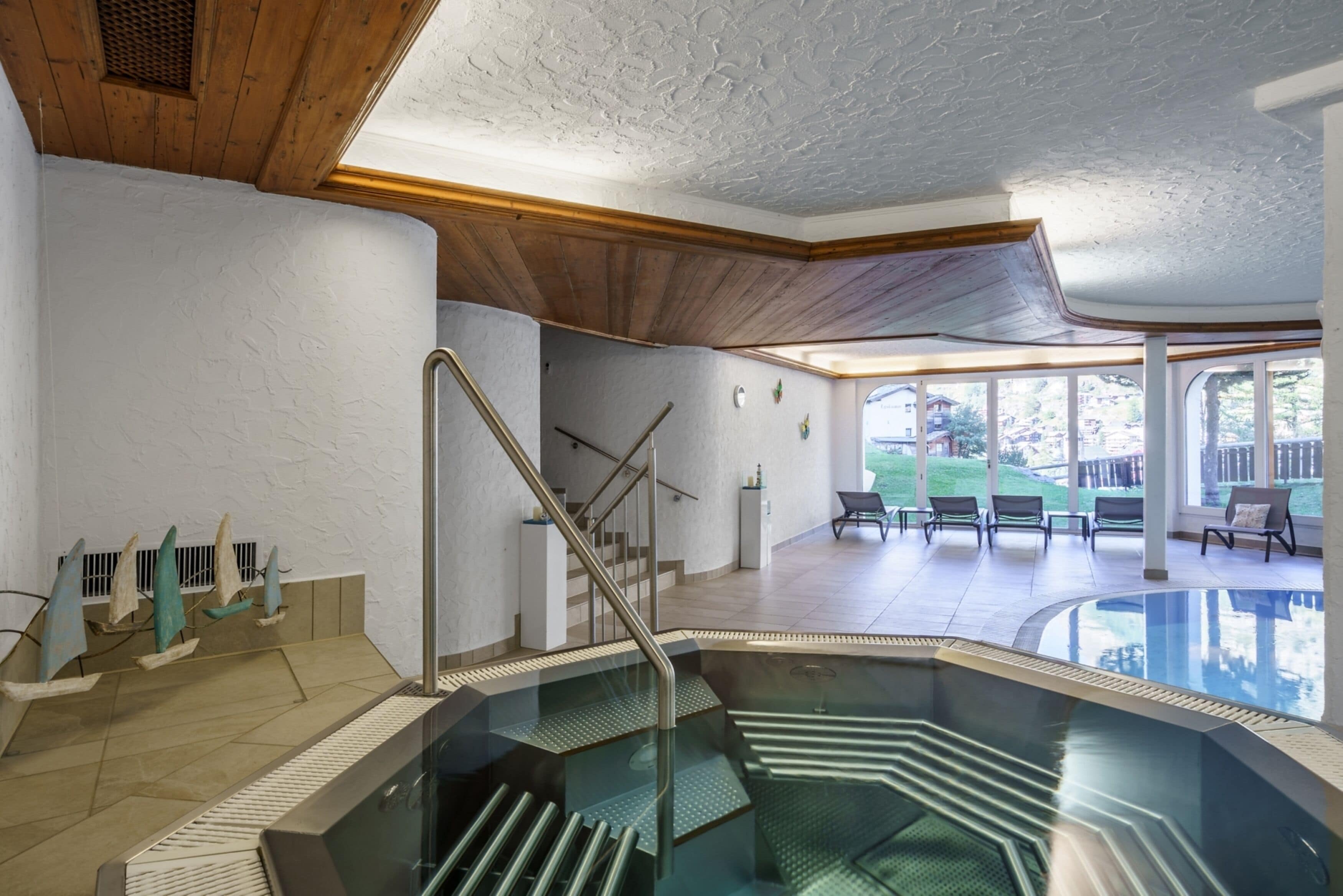 An indoor swimming pool with a glass barrier, wooden ceiling, and a view of the outside.