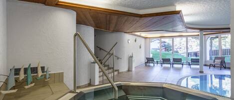 An indoor swimming pool with a glass barrier, wooden ceiling, and a view of the outside.