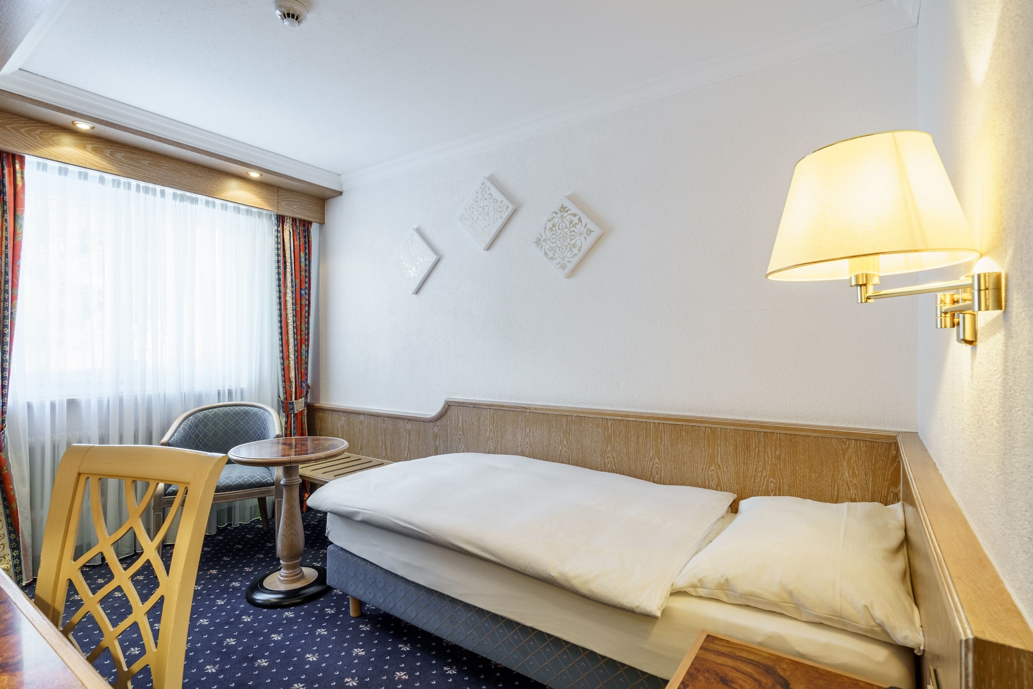 Une chambre d’hôtel avec un lit, une chaise, une petite table et une lampe.