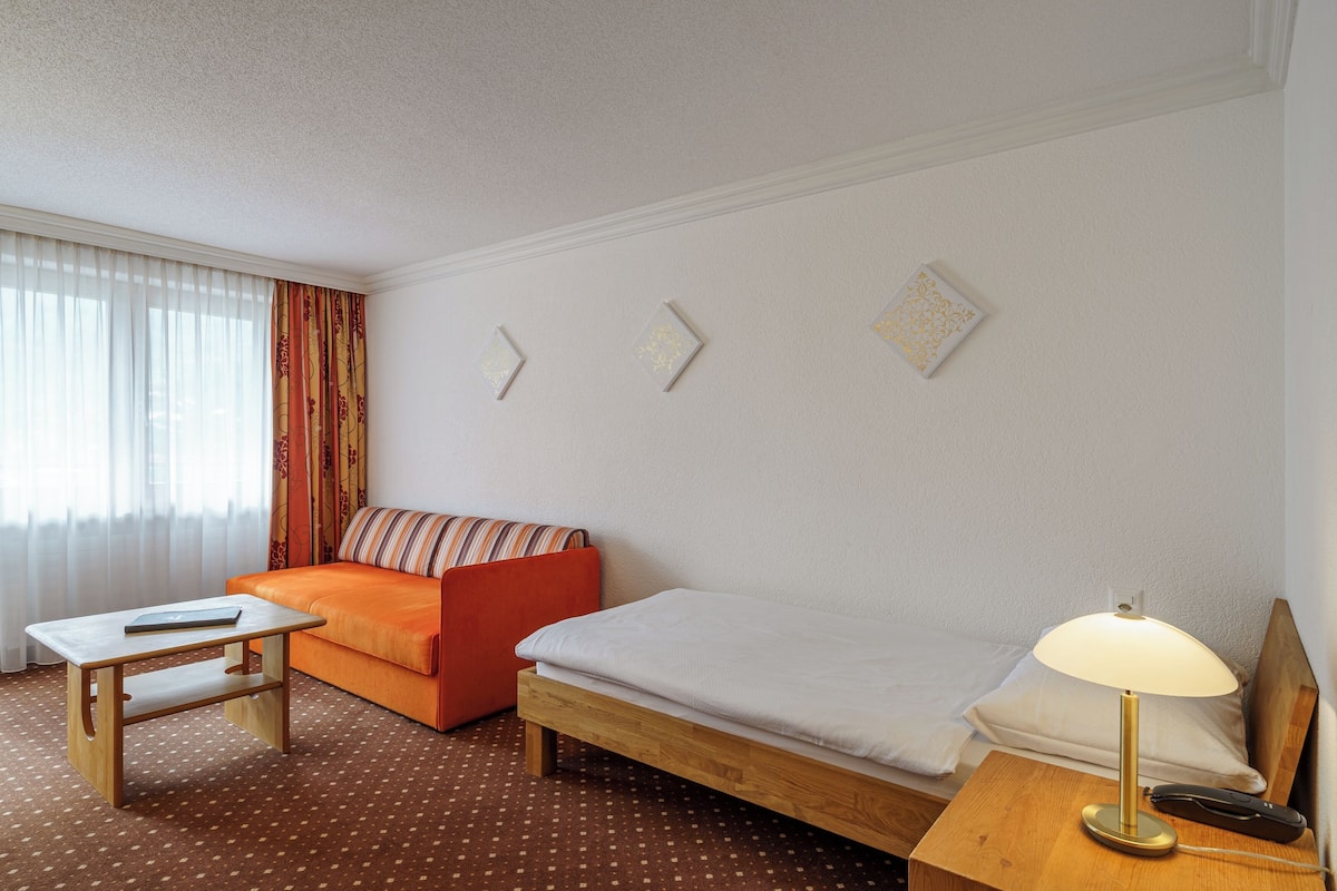 A hotel room with a wooden bed, a small table, an orange sofa, and a lamp.