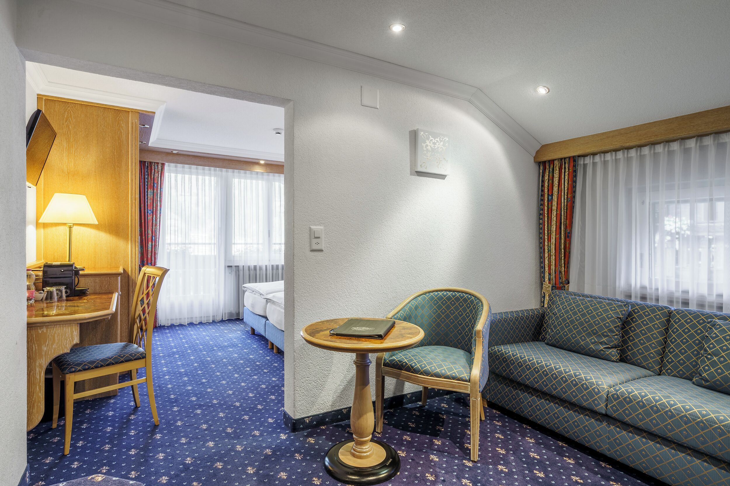 A hotel room with a dining area, a sofa, a small table, and a bed.
