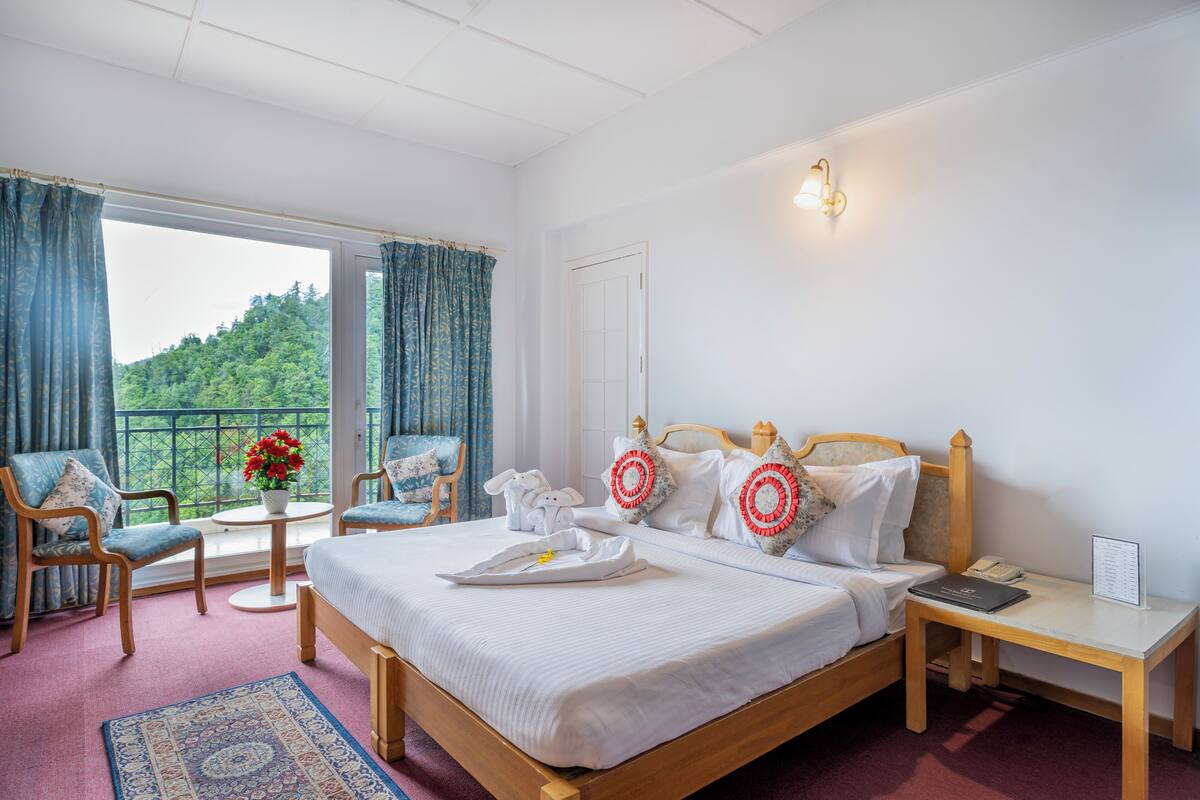 Habitación de hotel con cama, mesita de noche, silla, mesa y vista a zonas verdes.