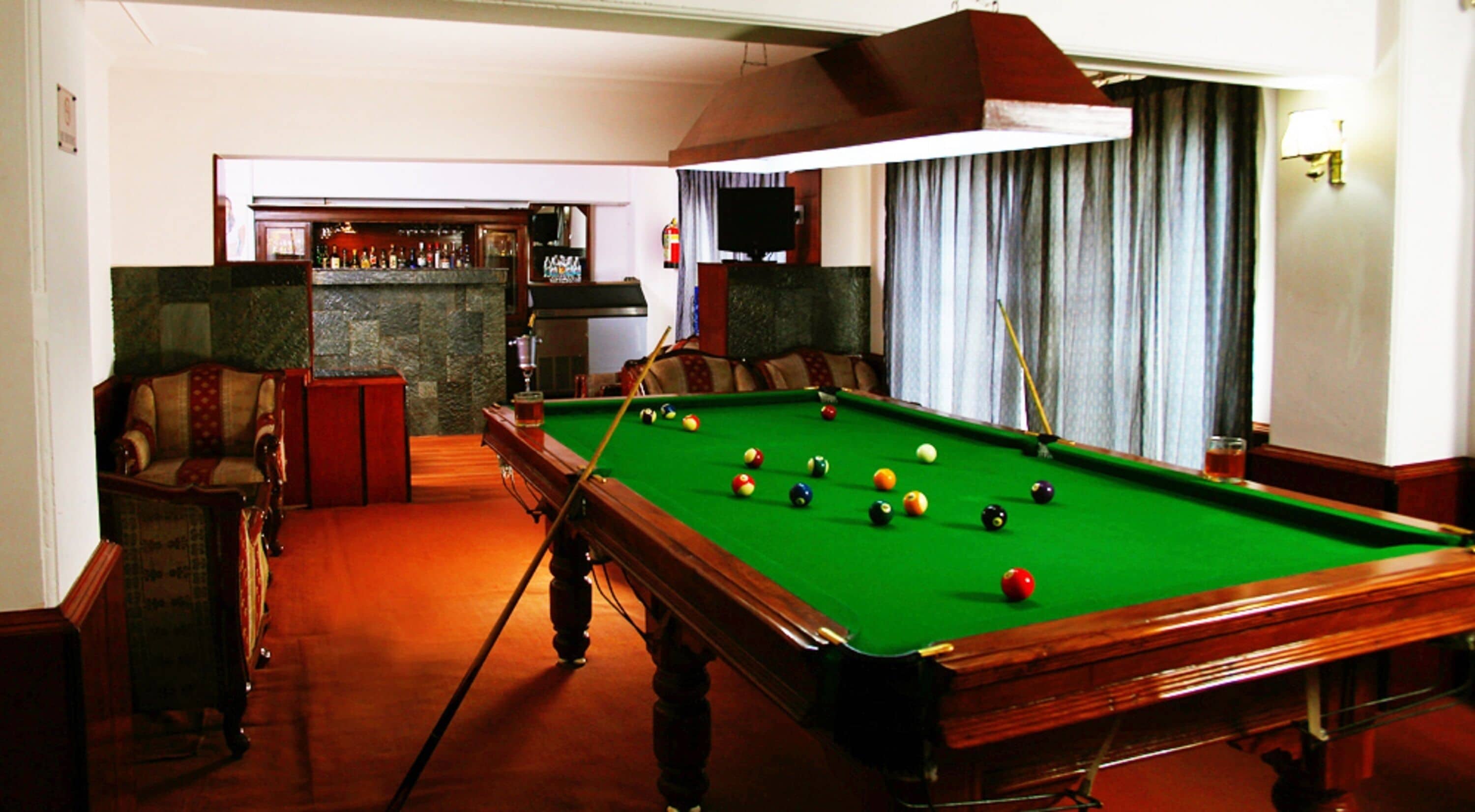 Mesa de billar con bolas, zona de bar y asientos.