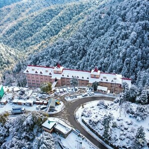 A large building with multiple floors, surrounded by snow-covered trees and a parking area. - Toshali Royal View Resort (Shimla)
