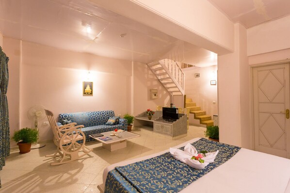 A hotel room with a bed, a sofa, a rocking chair, a coffee table, a TV, a staircase, and a door.