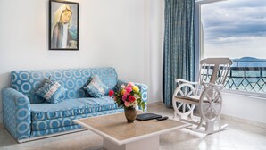 A room with a blue patterned sofa, a white rocking chair, a coffee table with a vase of flowers, and a painting on the wall. - Toshali Royal View Resort (Shimla)