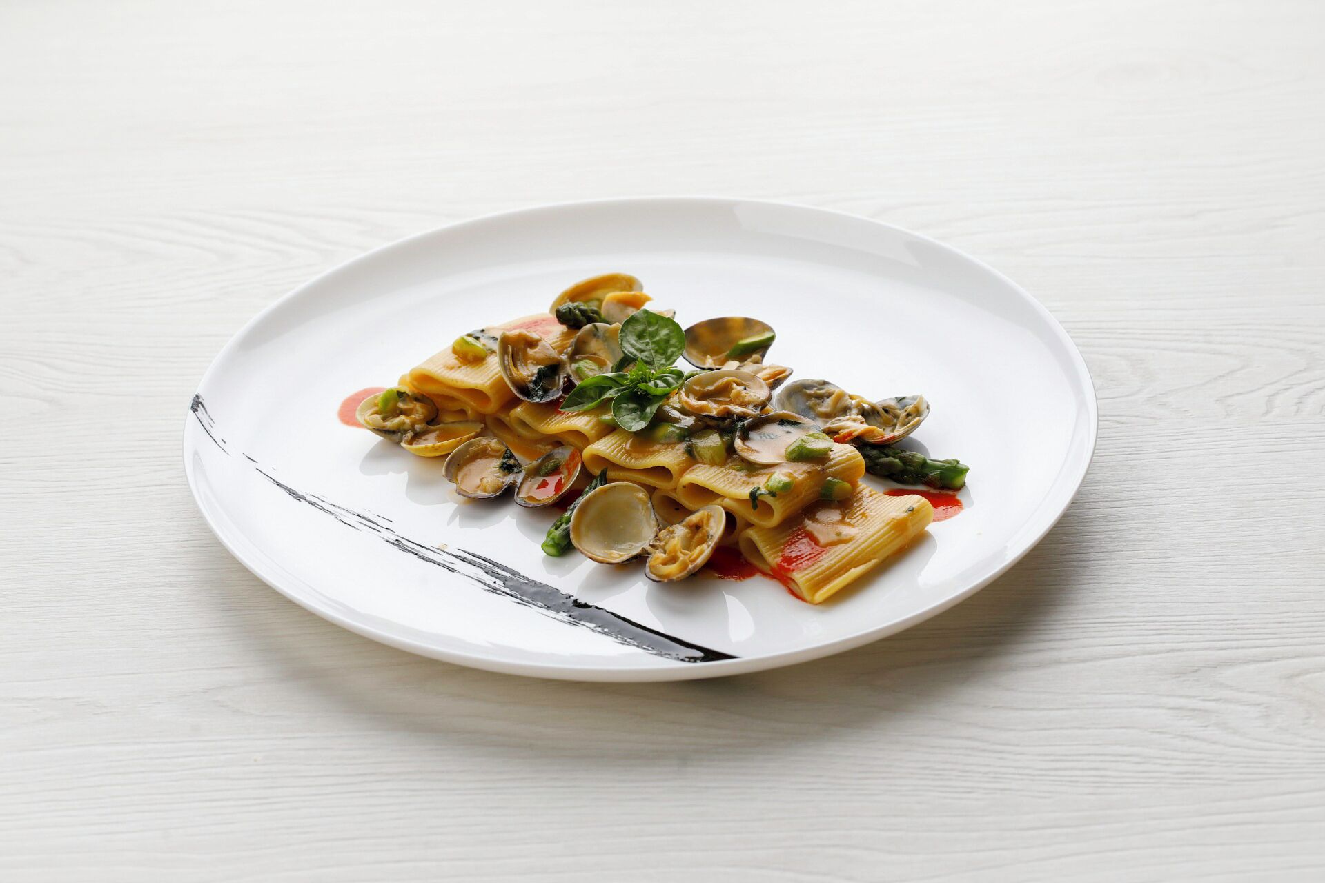 A plate of pasta with clams, asparagus, and spinach on a white plate.