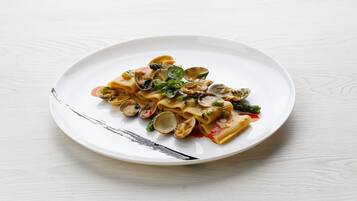 A plate of pasta with clams, asparagus, and spinach on a white plate.