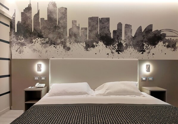 A hotel room with a bed, two bedside tables, a phone, and a city skyline mural on the wall. - The Sydney Hotel (Bologna)