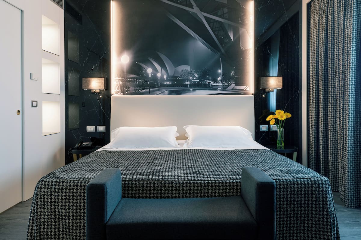 Une chambre d’hôtel moderne, dotée d’un grand lit, de deux tables de chevet et offrant une vue sur un bâtiment à l’architecture remarquable.