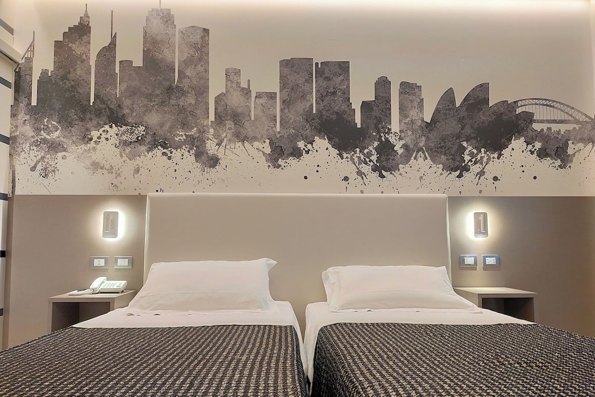 Une chambre d’hôtel avec deux lits, une fresque représentant le panorama de la ville sur le mur et des lampes de chevet.