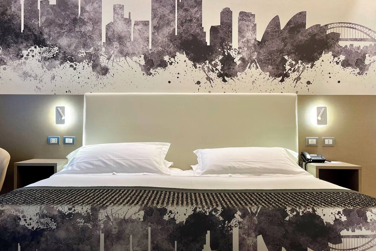Une chambre d’hôtel avec un lit, deux tables de chevet et une fresque murale représentant le panorama de la ville.
