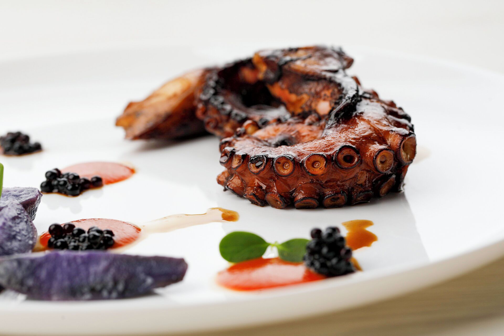 Un plato de pulpo a la parrilla con zarzamoras y salsa sobre una fuente blanca.