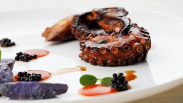 Un plato de pulpo a la parrilla con zarzamoras y salsa sobre una fuente blanca.
