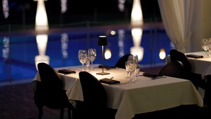 Een eettafel gedekt voor een maaltijd, met stoelen, en een zwembad op de achtergrond, verlicht met sfeerverlichting.