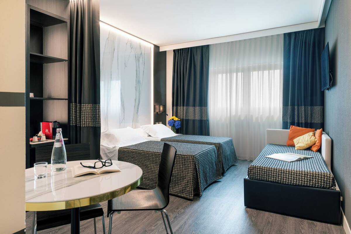 Une chambre d’hôtel moderne comprenant un lit, deux tables de chevet, une chaise, une petite table et une bibliothèque.