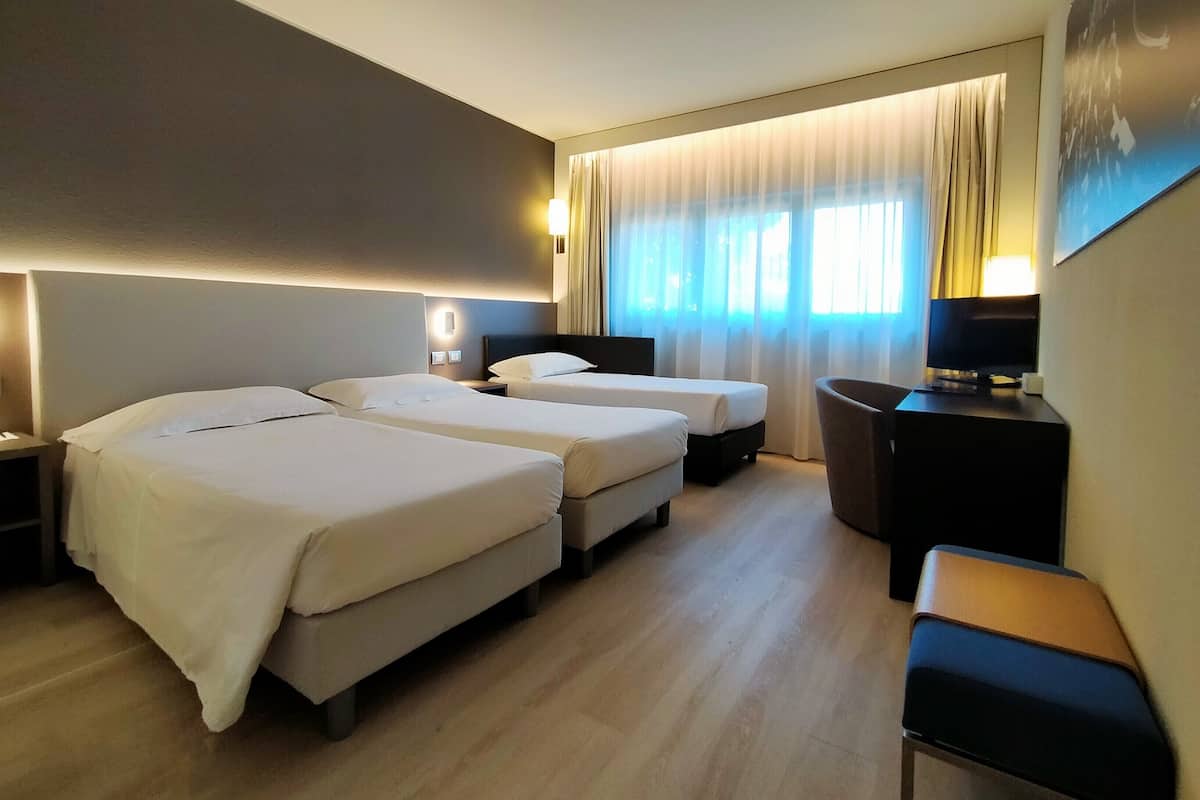 Une chambre d’hôtel avec deux lits, un bureau, une chaise et un téléviseur.