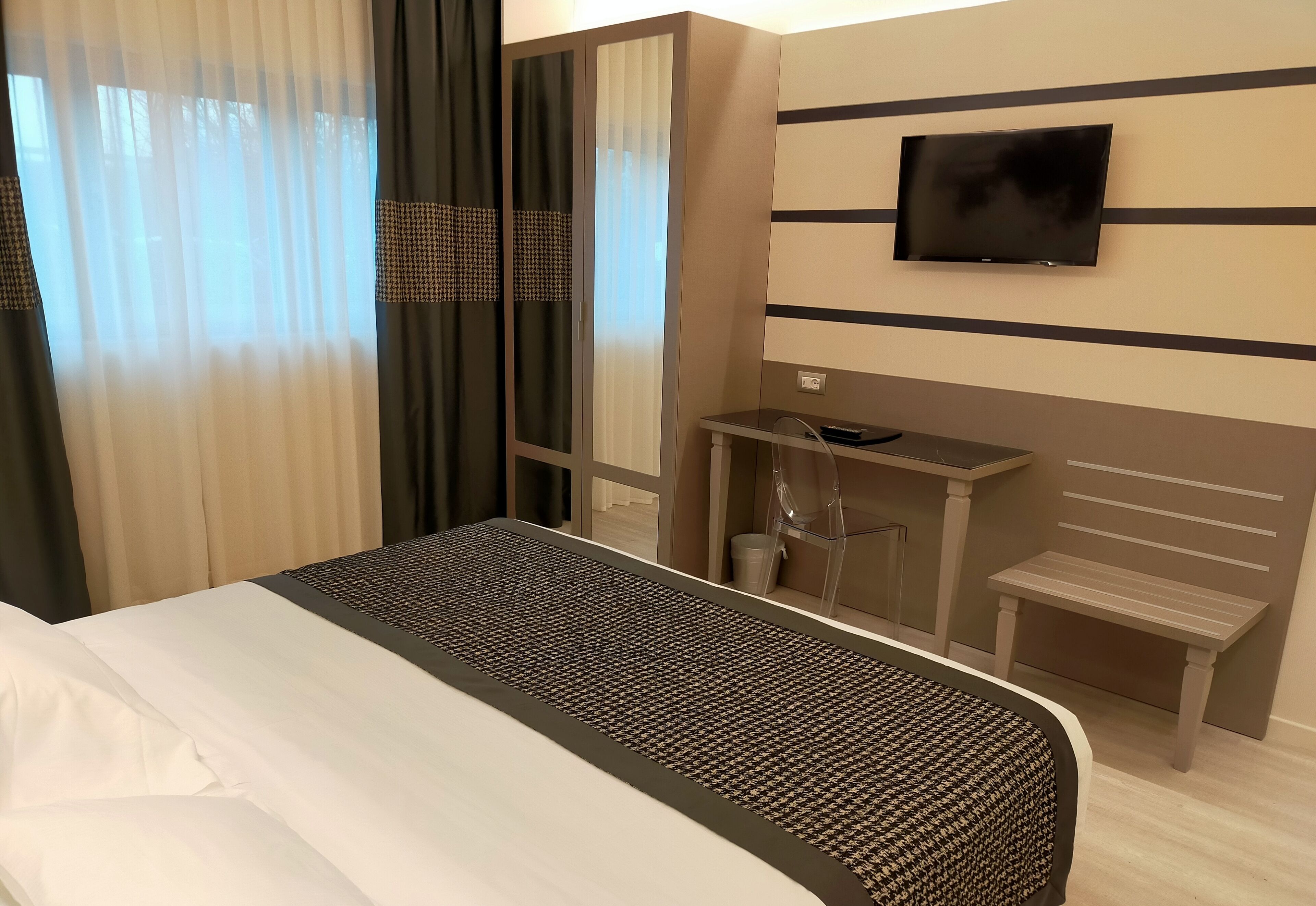Een hotelkamer met een bed, een aan de muur bevestigde televisie, een klein bureau en een bankje.