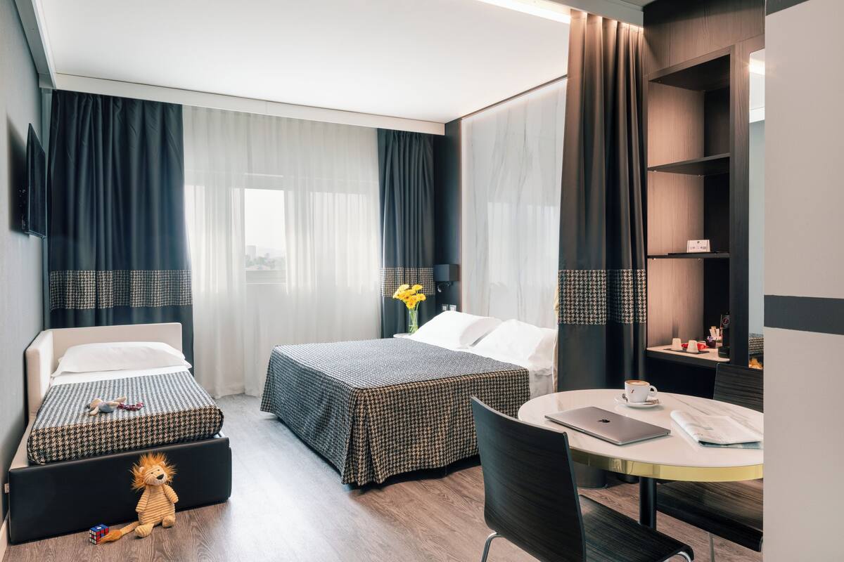 Une chambre d’hôtel avec deux lits, un bureau avec un ordinateur portable, une chaise et une petite table avec une tasse et une soucoupe.