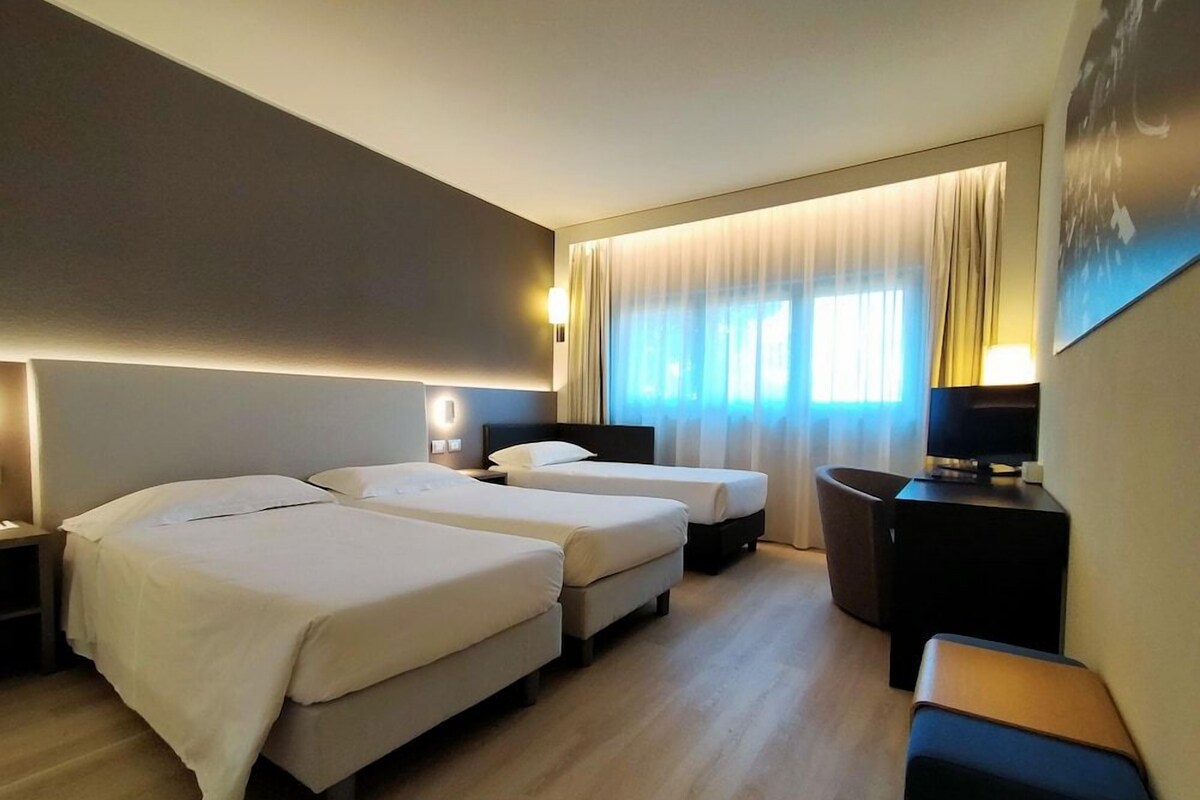 Une chambre d’hôtel avec deux lits, un bureau avec un ordinateur et une télévision.
